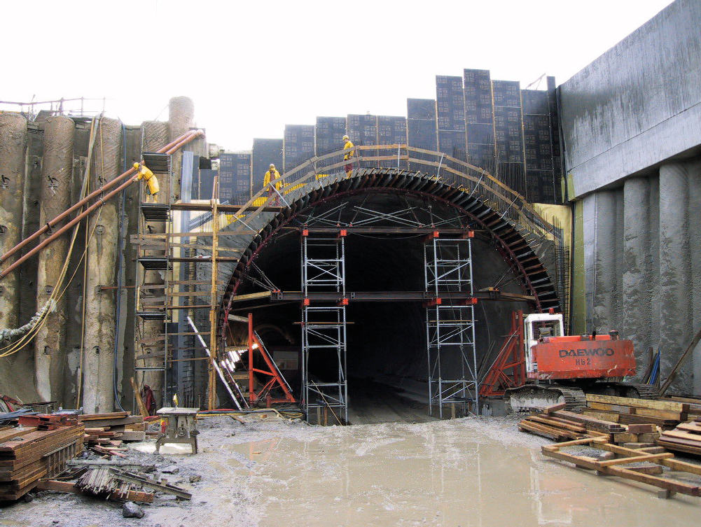 Foto: Tunneleinfahrt mit Gerüst, Bagger, im Vordergrund schlammiger Boden