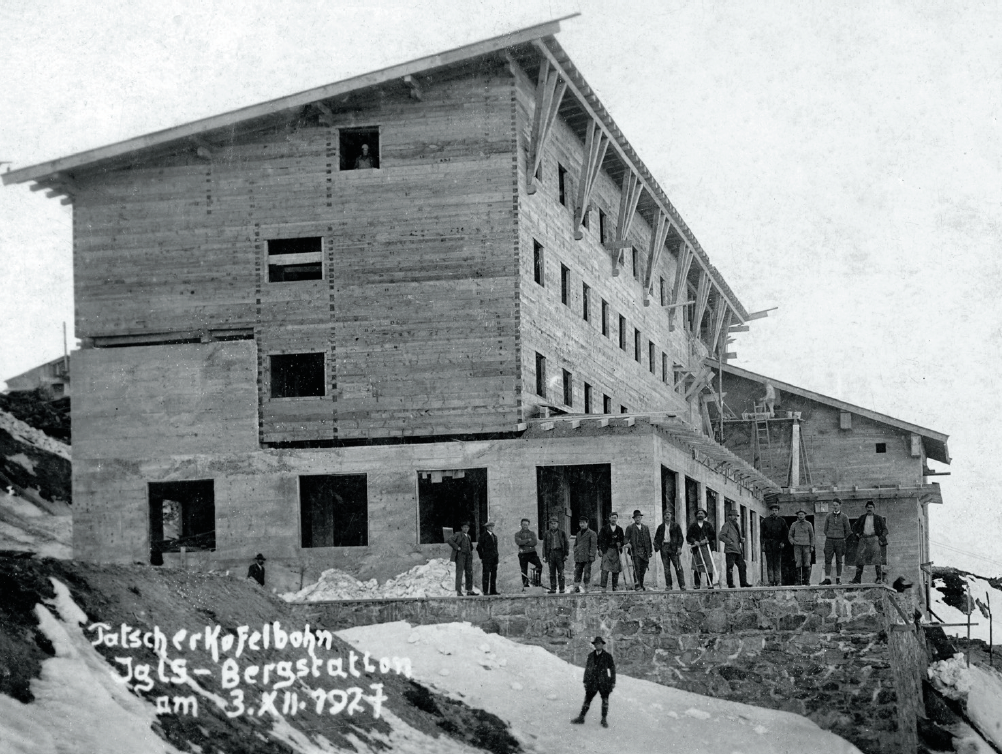 Historische Schwarz-Weiß-Aufnahme voder aus Holz errichteten Bergstation am Patscherkofel, davor aufgereiht mehrere Menschen